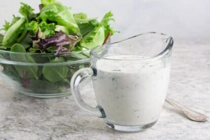 Low FODMAP Ranch Dressing in clear glass pitcher; green salad in background