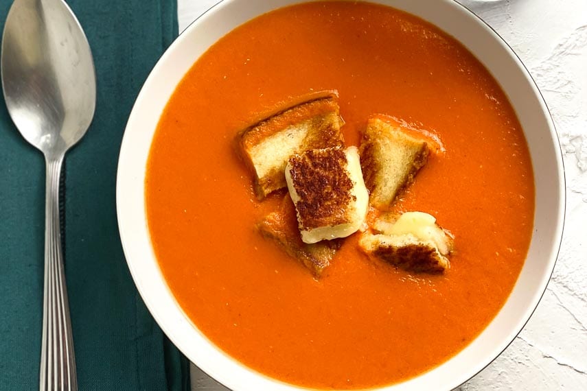 closeup Low FODMAP Cream of Tomato Soup in white bowl; teal napkin