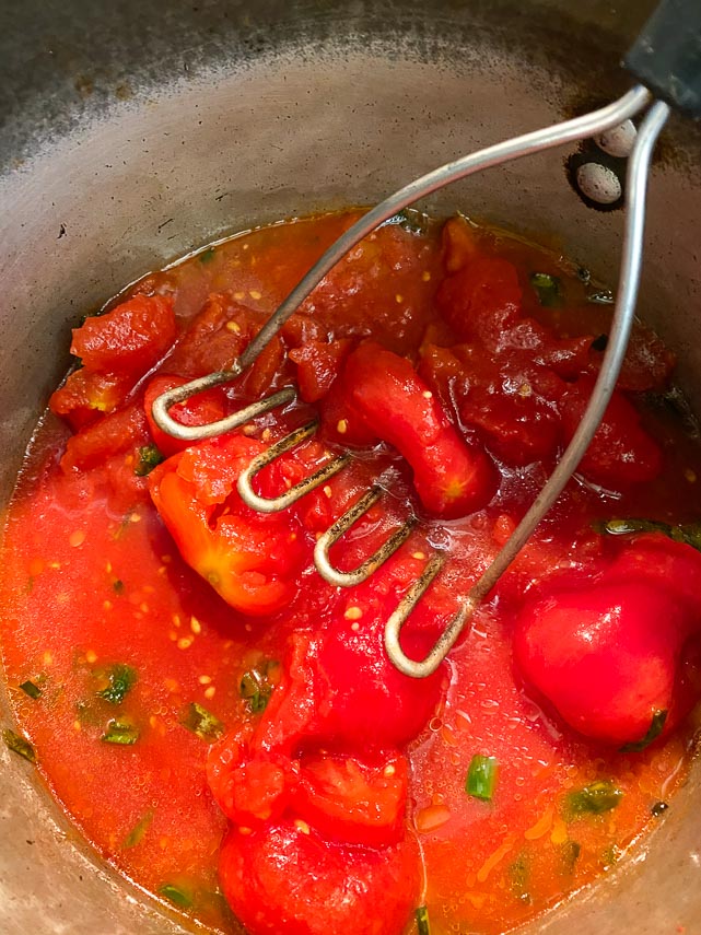 crushing tomatoes with potato masher