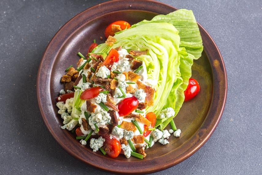 Low FODMAP Wedge Salad with bacon and tomatoes on ceramic brown plate and blue cheese dressing