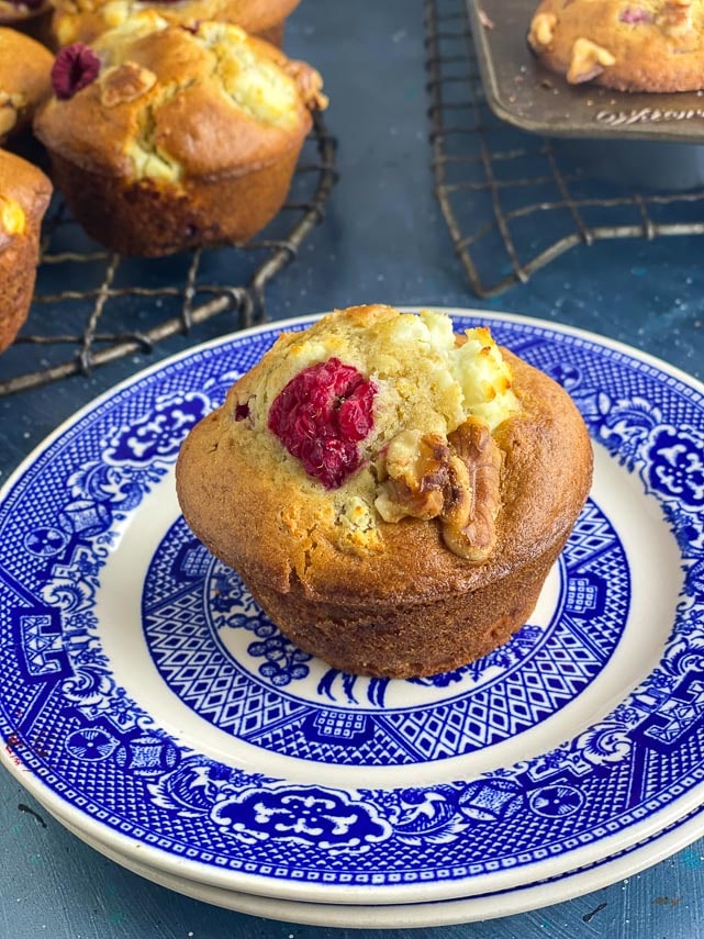 closeup of Low FODMAP Olive Oil Muffins with Goat Cheese, Walnuts and Raspberries in a round antique cooling rack; blue backdrop and blue plate