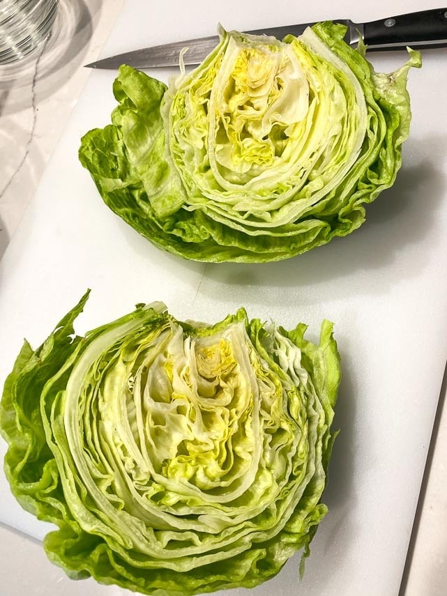 cut Iceberg lettuce head in half, on white cutting board