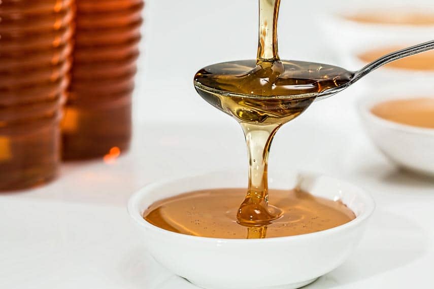 honey pouring into a spoon, overflowing into a white bowl