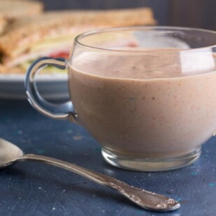 horizontal image of Low FODMAP Russian Dressing in a clear glass bowl with handles; blue backdrop
