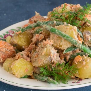 horizontal image of low FODMAP Salmon Potato Salad with green beans and dill sprigs on white oval platter; blue background