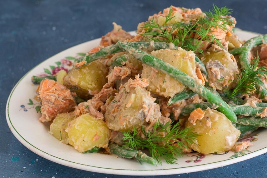 horizontal image of low FODMAP Salmon Potato Salad with green beans and dill sprigs on white oval platter; blue background