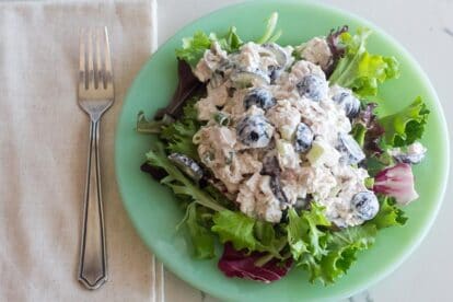 overhead horizontal image of Low FODMAP Chicken Salad with Grapes and Almonds on a bed of lettuce on a green plate; fork and linen napkin alongside