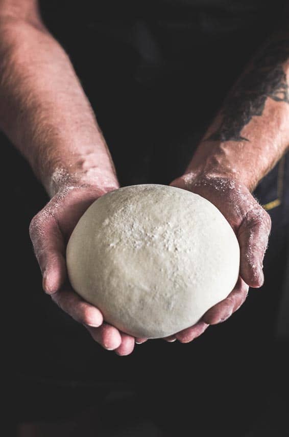 raw bread dough in man's hands; dark background