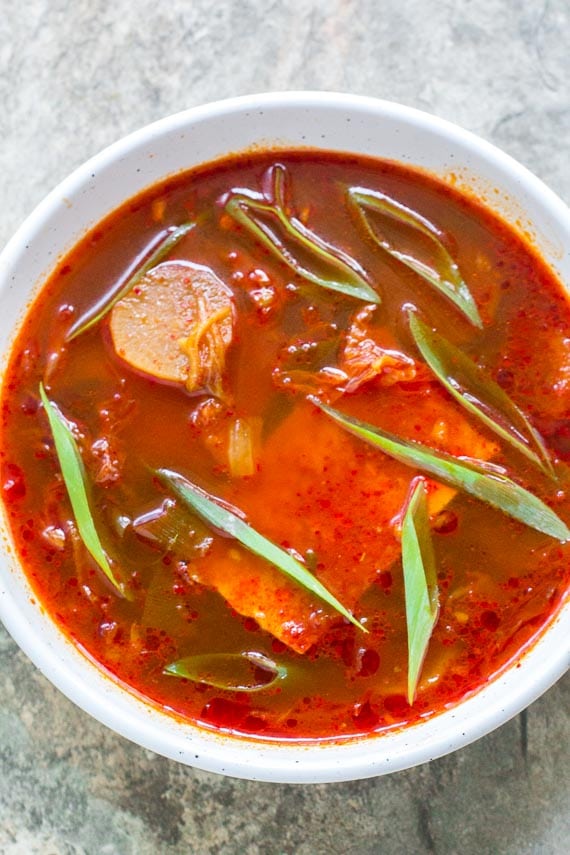 vertical image of low FODMAP Kimchi and Tofy stew in white bowl on stone surface