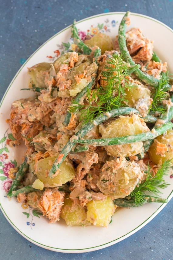 vertical image of low FODMAP Salmon Potato Salad with green beans and dill sprigs on white oval platter; blue background
