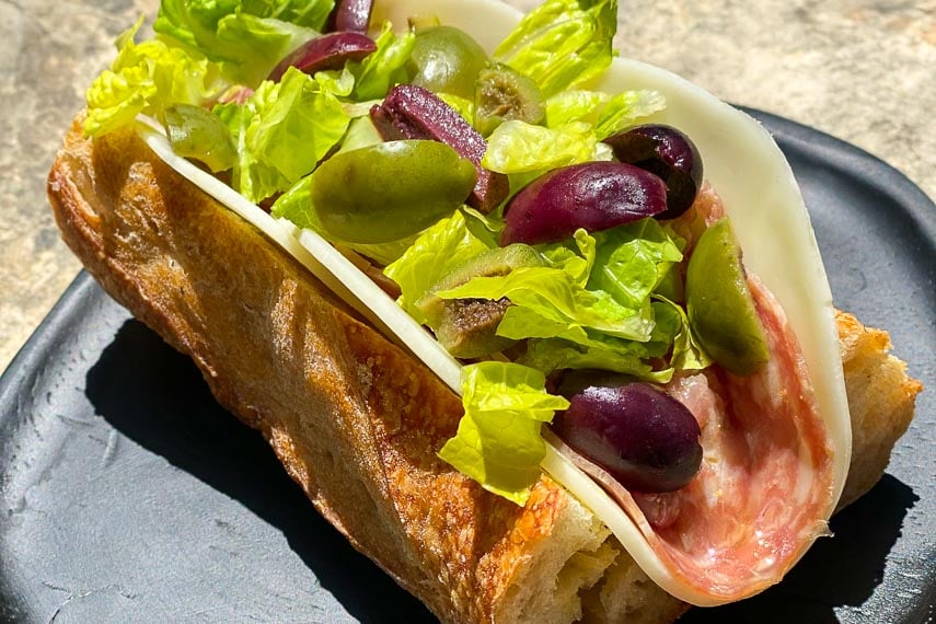 CLOSEUP Low FODMAP Italian Sub on a black woode plate, outside on stone surface; heavy shadows across plate