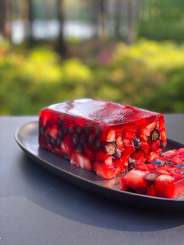 Low FODMAP Mixed Berry Terrine on an oval black plate; outside on deck - garden in background