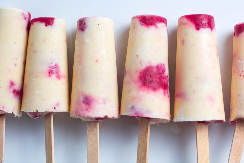 Low FODMAP peaches & cream popsicles with raspberries, close up, lined up on white plate_