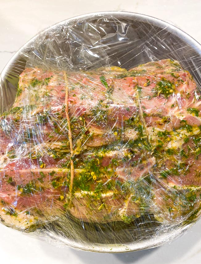 Porchetta Pork roast coated with wet marinade, wrapped up with plastic wrap, ready to refrigerate overnight