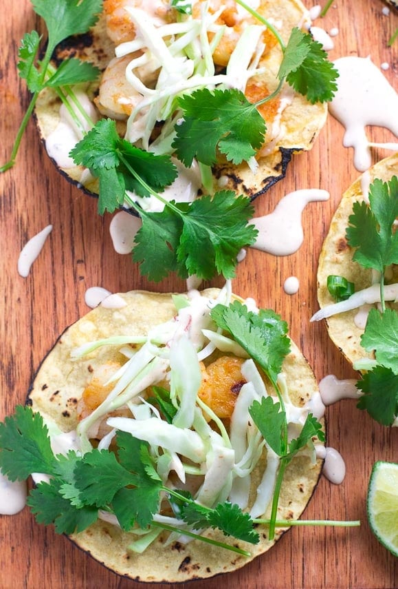 Vertical closeup image Low FOMAP Shrimp Tacos with Lime Crema on wooden board; wedges of lime alongside