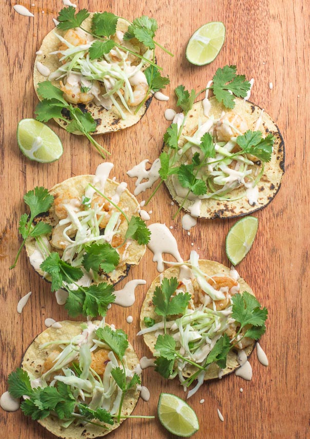 Vertical image Low FOMAP Shrimp Tacos with Lime Crema on wooden board; wedges of lime alongside