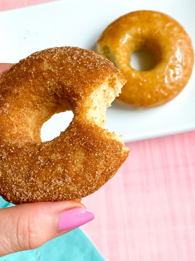 a bite taken out of Low FODMAP Baked Doughnuts, coated in cinnamon-sugar, held in manicured hand