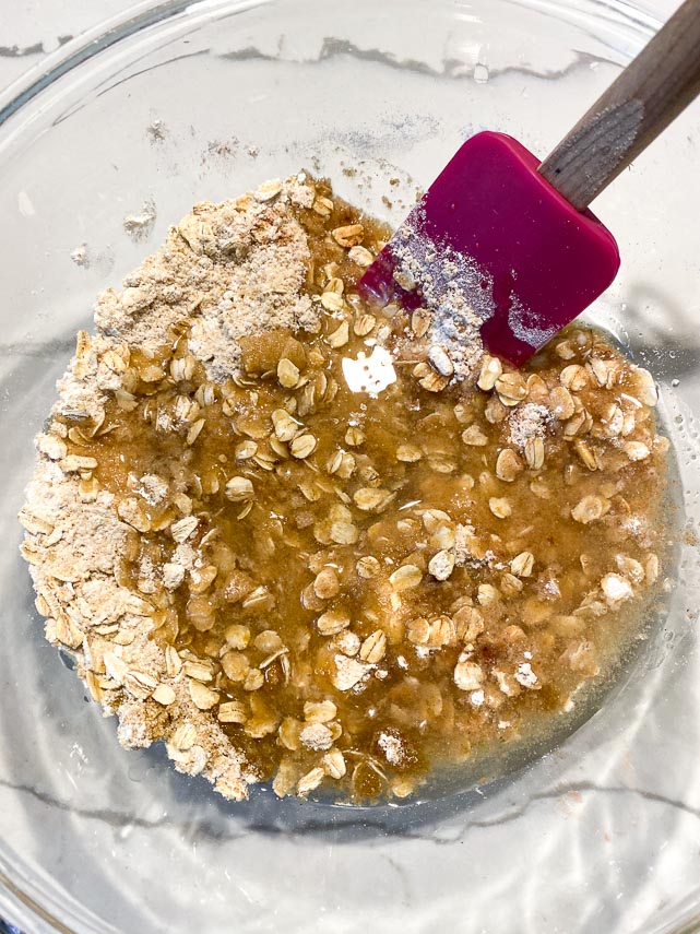adding melted coconut oil to Vegan Low FODMAP Crisp Topping dry ingredients in a glass bowl