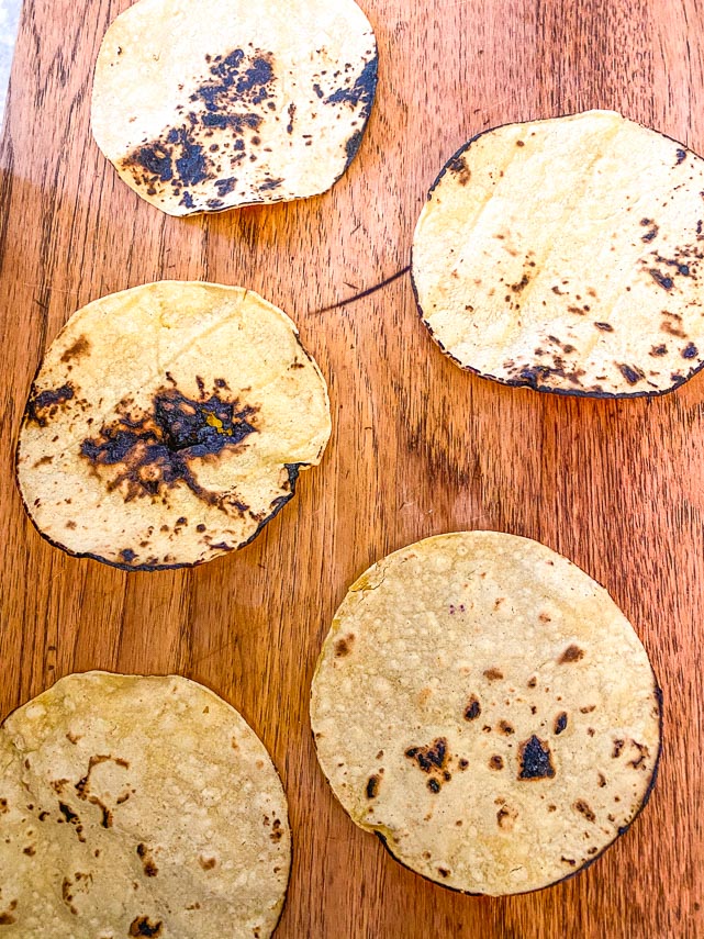 charred corn tortillas on a wooden board, ready for shrimp tacos