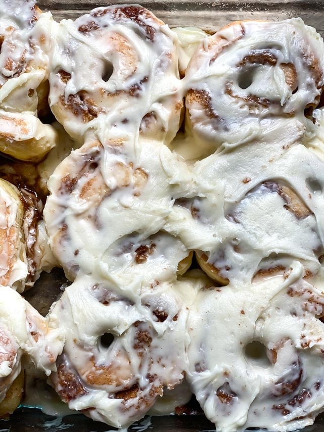 closeup cream cheese frosted cinnamon roll in glass pan