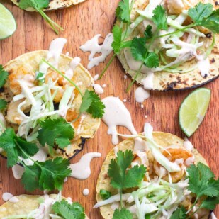 closeup image Low FOMAP Shrimp Tacos with Lime Crema on wooden board; wedges of lime alongside