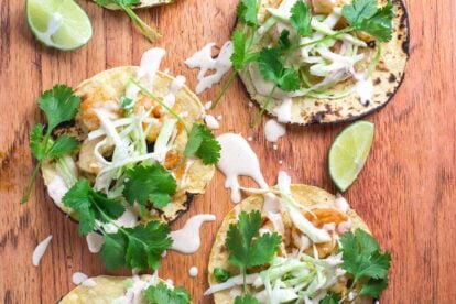 closeup image Low FOMAP Shrimp Tacos with Lime Crema on wooden board; wedges of lime alongside