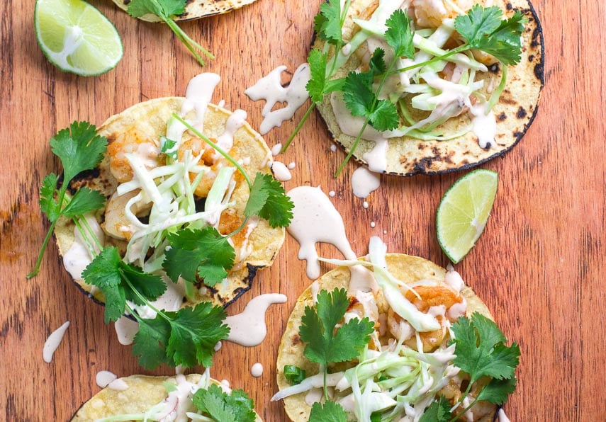 closeup image Low FOMAP Shrimp Tacos with Lime Crema on wooden board; wedges of lime alongside