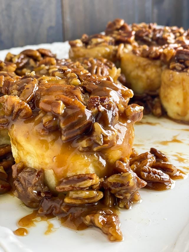 closeup of low FODMAP gluten-free caramel pecan sticky buns on white plate, nuts spilling down side