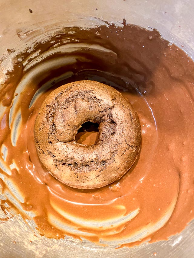 dipping a chocolate doughnut in a cocoa glaze