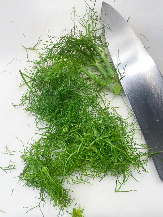fennel fronds on cutting board with chef's knife