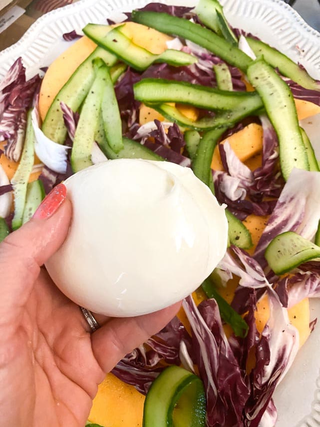 holding a ball of burrata over a salad