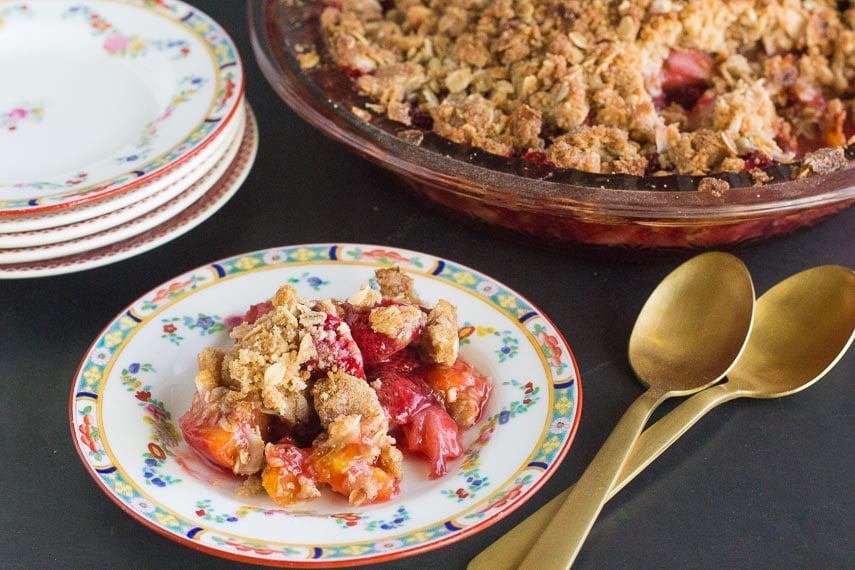 horizontal image of low FODMAP strawberry peach crisp on a decorative plate and in pie plate in background