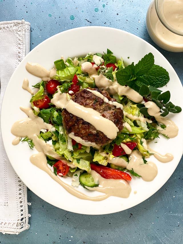 low FODMAP lamb burgers with tahini sauce on white plate and blue table