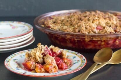 low FODMAP strawberry peach crisp on a decorative plate and in pie plate in background; gold colored spoons