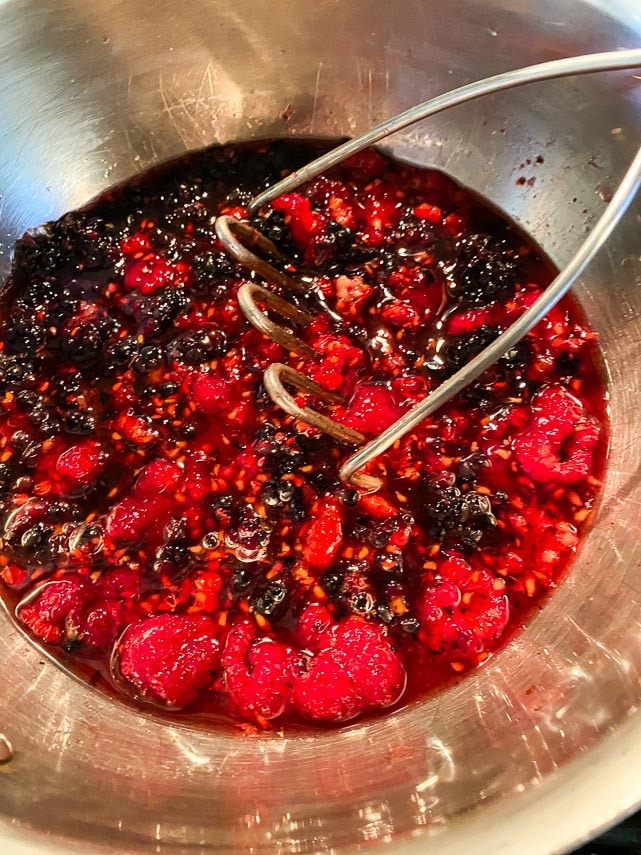 mashing berries with a potato masher for sauce