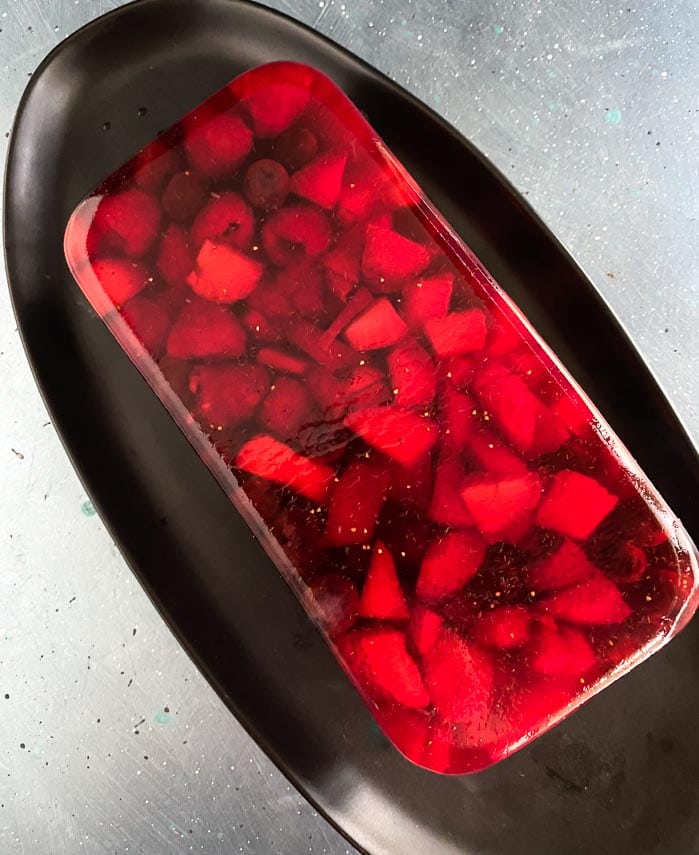 overhead of Low FODMAP Mixed Berry Terrine on an oval black plate; blue surface