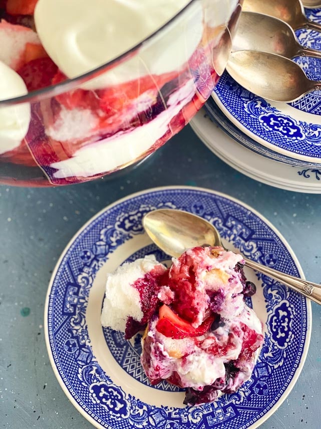 overhead vertical image of Low FODMAP Red, White & Blue Trifle in clear glass trifle bowl; individual serving on blue plate alongside with silver spoon