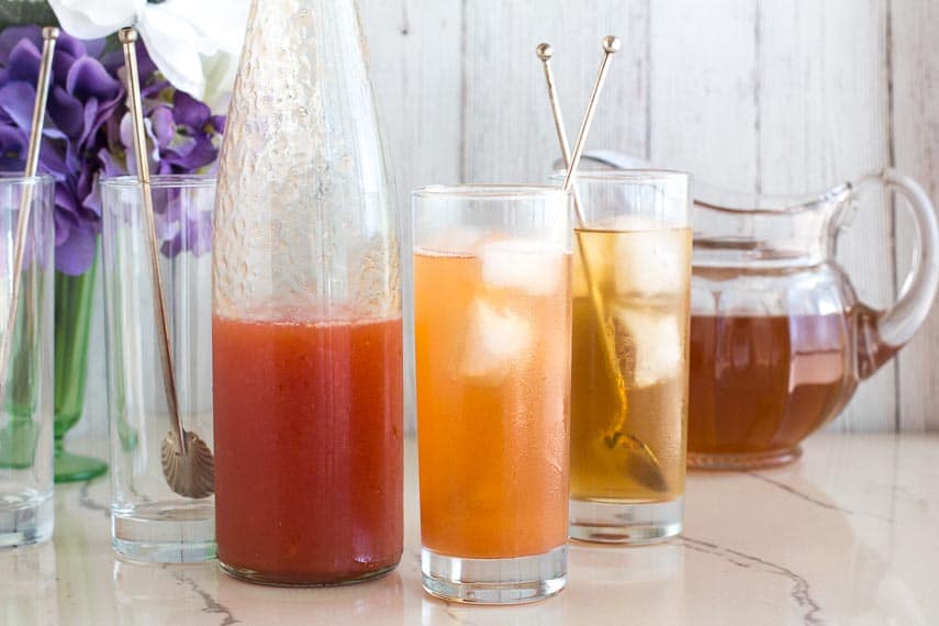 peach iced tea in tall glasses with silver spoons against white backdrop_