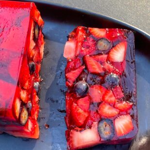 slice of Low FODMAP Mixed Berry Terrine on an oval black plate; outside on deck in sunlight