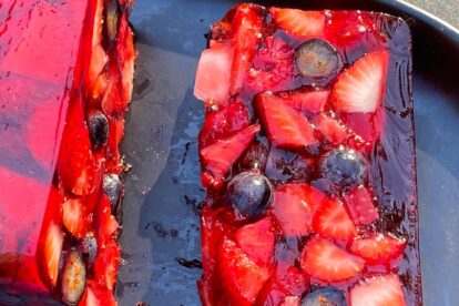 slice of Low FODMAP Mixed Berry Terrine on an oval black plate; outside on deck in sunlight