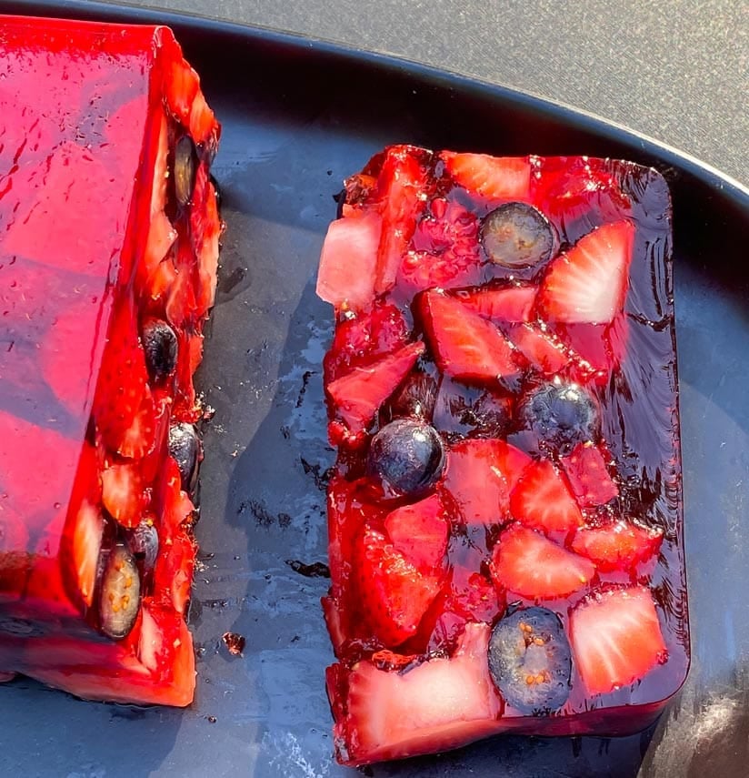 slice of Low FODMAP Mixed Berry Terrine on an oval black plate; outside on deck in sunlight