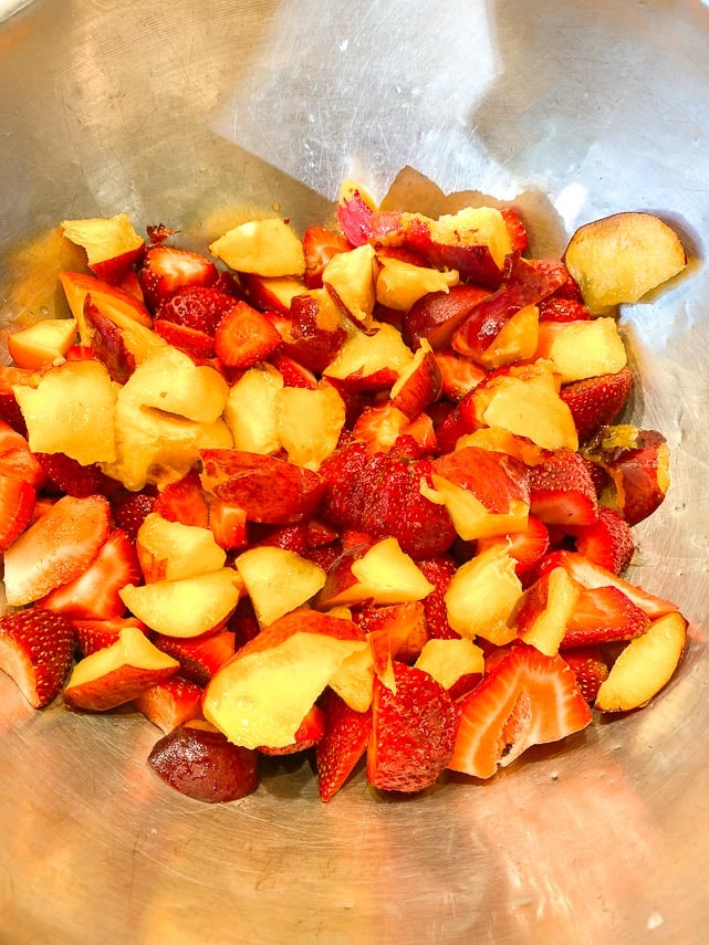 tossing strawberries and peaches together in a metal bowl for crisp
