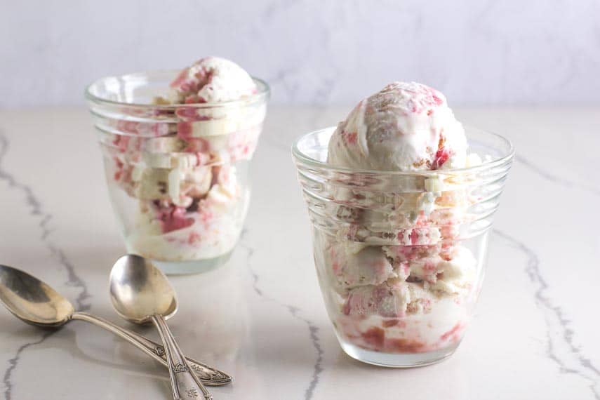 two glass dishes holding low FODMAP Rhubarb Crumble Ice Cream; silver spoons alongside on a white marble counter