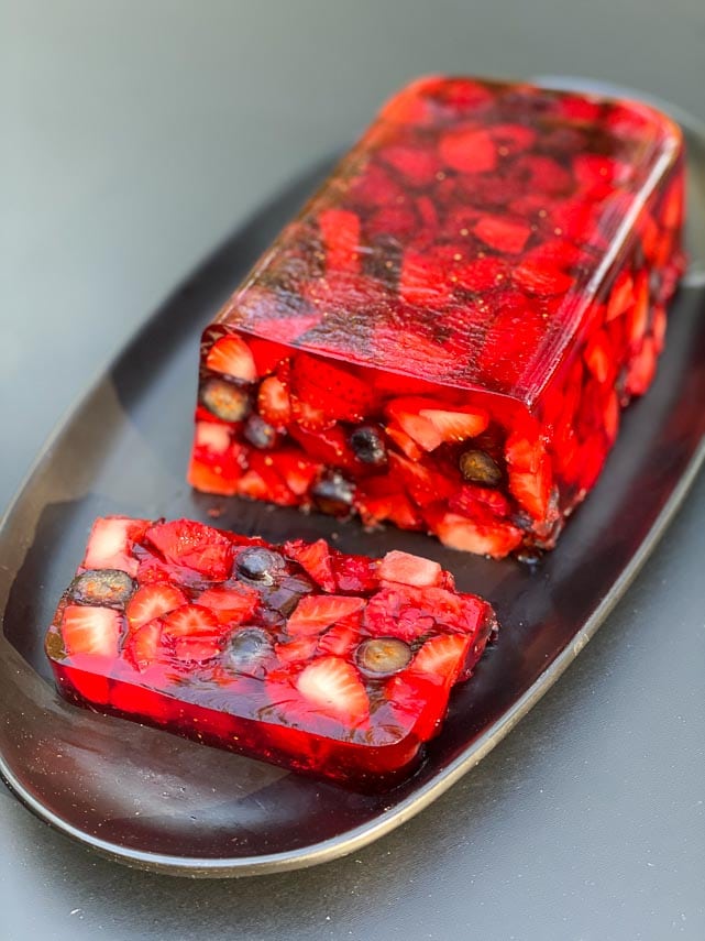 vertical image of Low FODMAP Mixed Berry Terrine on an oval black plate; outside in sun