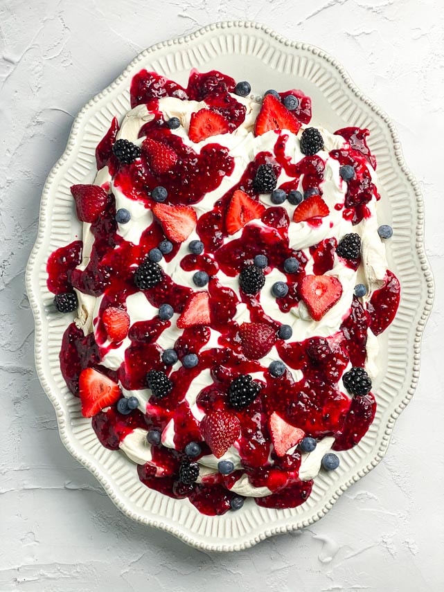 vertical image of low FODMAP Mixed Berry Slab Pavlova on decorative oval plate; white background