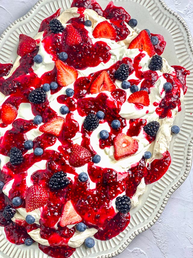 vertical image of low FODMAP Mixed Berry Slab Pavlova on oval plate; white background