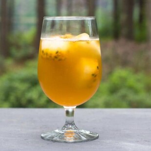 Low FODMAP Iced Green tea with Passionfruit in a clear footed glass on gray surface; outdoors