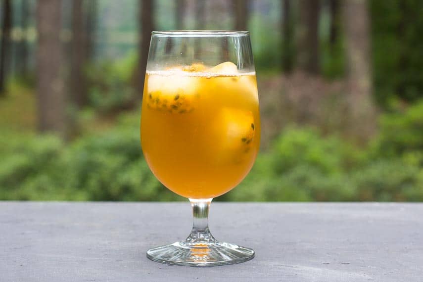 Low FODMAP Iced Green tea with Passionfruit in a clear footed glass on gray surface; outdoors