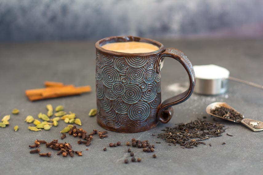 Low FODMAP Masala Chai in a decorative mug on dark surface surrounded by spices, tea and sugar