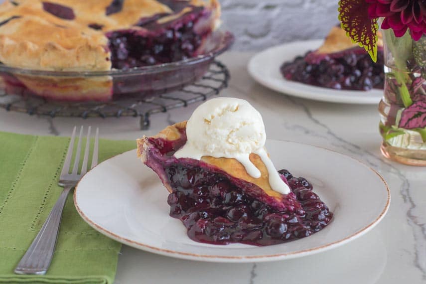 Low FODMAP No Churn Vanilla Ice cream melting on a wedge of blueberry pie on a white plate